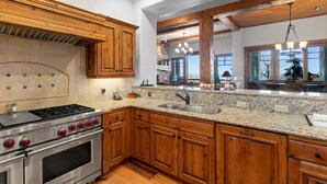 A kitchen with wooden cabinets, granite countertops, a stainless steel stove, and a large window overlooking a scenic view. - Grand Lodge - 3 Bedroom Condo Deluxe #206 - Ski-in/out by Deer Valley Resort (Park City)