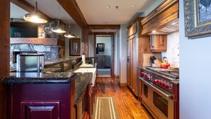 A kitchen with wooden cabinets, a stone fireplace, and a stainless steel range hood. - Grand Lodge - Three Bedroom Condo #301 - Ski-in/ski-out by Deer Valley Resort (Park City)