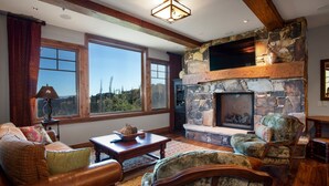 A cozy living room with a stone fireplace, large windows, and rustic wooden beams. - Grand Lodge - Three Bedroom Condo #301 - Ski-in/ski-out by Deer Valley Resort (Park City)