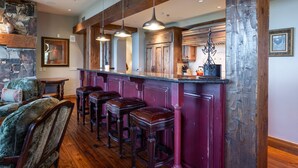 A bar area with wooden bar stools, pendant lighting, and a stone wall. - Grand Lodge - Three Bedroom Condo #301 - Ski-in/ski-out by Deer Valley Resort (Park City)