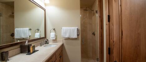 A bathroom with a large mirror, two sinks, a shower, and wooden cabinets.