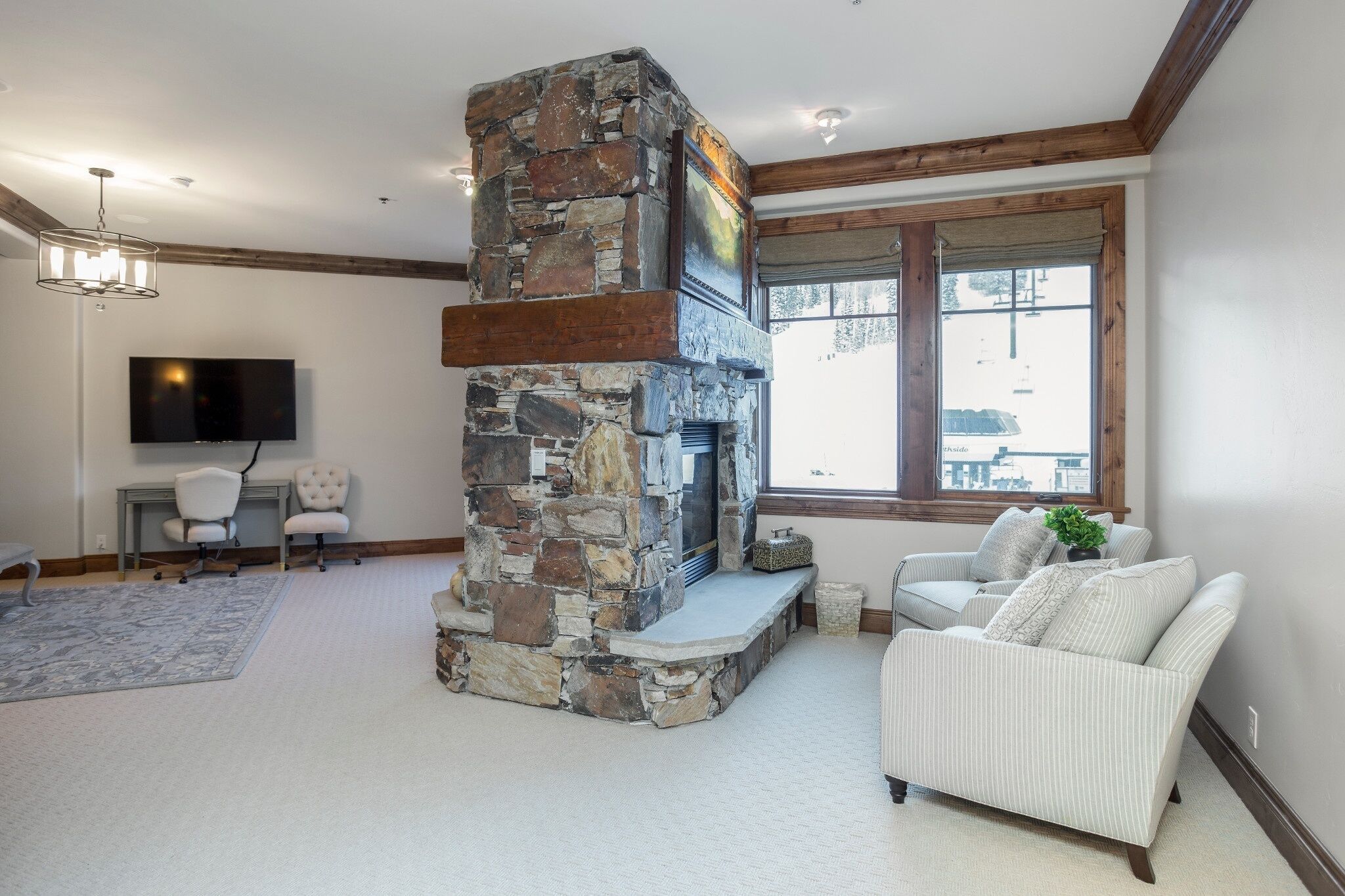 A living room with a stone fireplace, a television, and two white armchairs.