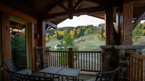 A wooden deck with a table and chairs, overlooking a forested hillside. - Grand Lodge - Five Bedroom Condo #402 - Ski-in/ski-out by Deer Valley Resort (Park City)