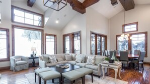 A spacious living room with a sectional sofa, a coffee table, and a dining area with chairs and a table. - Grand Lodge - Five Bedroom Condo #402 - Ski-in/ski-out by Deer Valley Resort (Park City)
