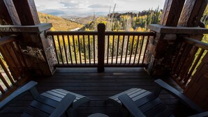 A wooden deck with Adirondack chairs and a table, overlooking a mountainous landscape with autumn foliage.