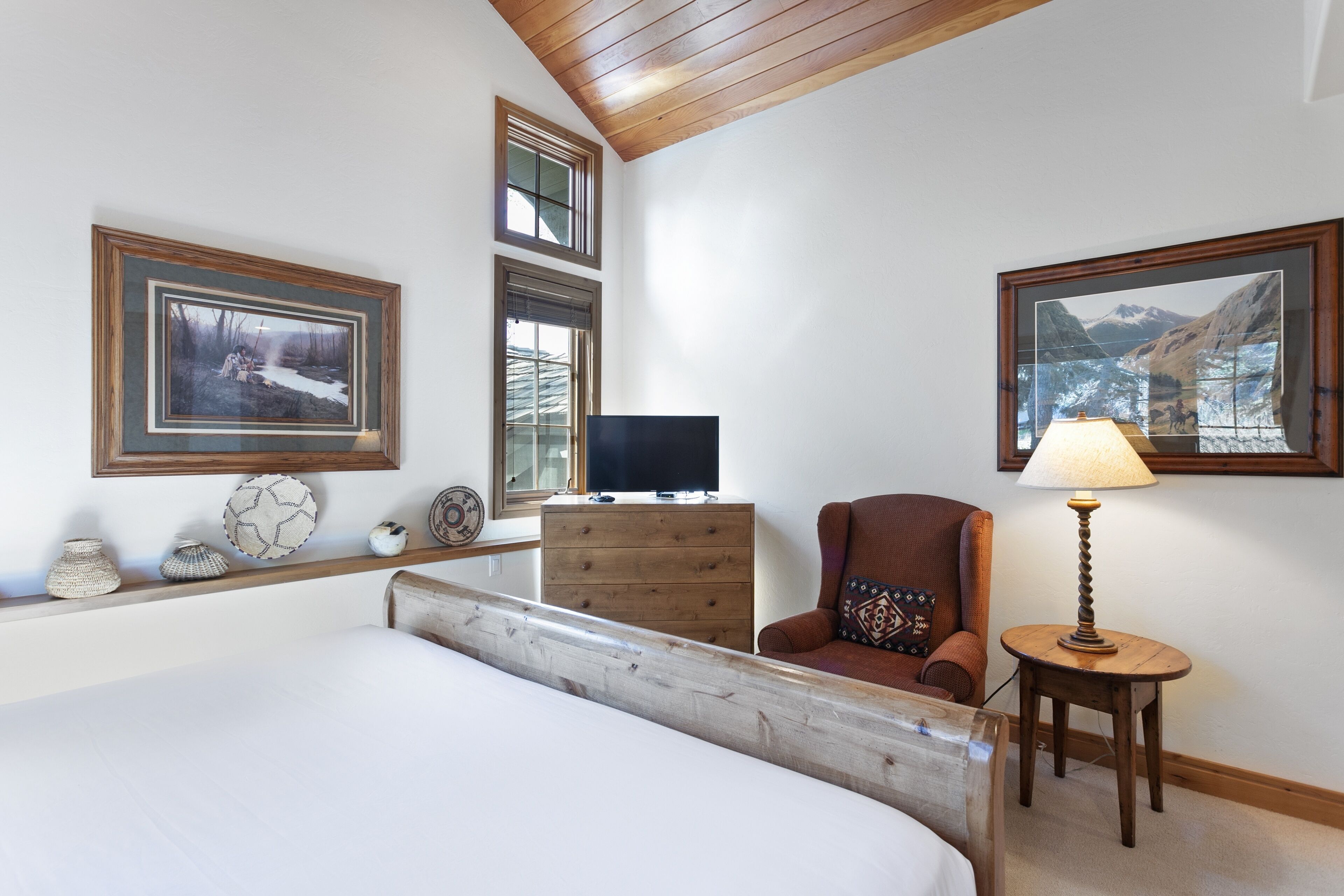 A bedroom with a large bed, wooden dresser, armchair, and a television on a wooden stand.