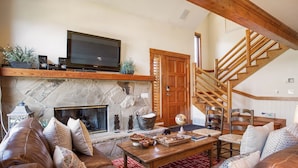 A cozy living room with a stone fireplace, leather sofa, wooden coffee table, and a TV on a wooden shelf. - Deer Lake Village at Deer Valley Resort - Four Bedroom Condo with Hot Tub #2477 4 Condo (Park City)