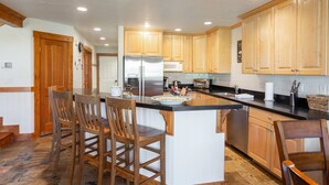 A modern kitchen with wooden cabinets, a stainless steel refrigerator, a microwave, and a large island with bar stools. - Deer Lake Village at Deer Valley Resort - Four Bedroom Condo with Hot Tub #2477 4 Condo (Park City)