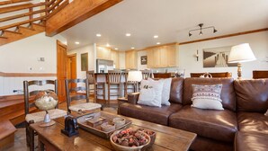 A spacious living area with a brown leather sofa, wooden coffee table, and a globe. A staircase leads to an upper level. - Deer Lake Village at Deer Valley Resort - Four Bedroom Condo with Hot Tub #2477 4 Condo (Park City)