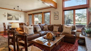 A spacious living room with a large brown leather sofa, wooden coffee table, and a dining area with chairs and a table. - Deer Lake Village at Deer Valley Resort - Four Bedroom Condo with Hot Tub #2477 4 Condo (Park City)