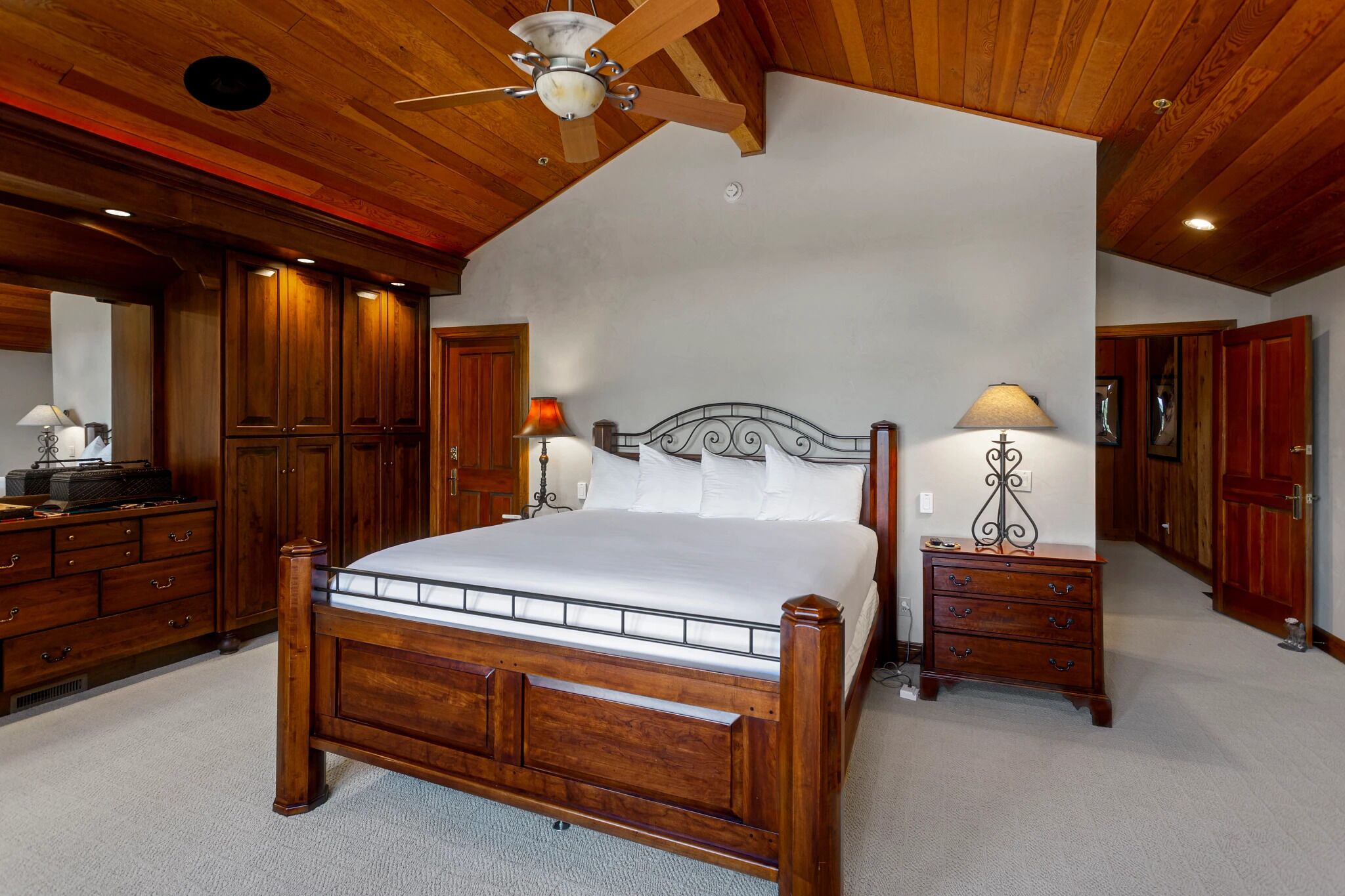 Un dormitorio espacioso con una cama de madera grande, armarios de madera y un ventilador de techo.