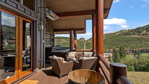 Un patio in legno con arredi da esterno, una vasca idromassaggio e vista su un paesaggio montuoso.