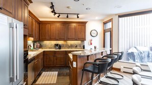 A kitchen with wooden cabinets, a stainless steel refrigerator, a coffee maker, and a bar area with bar stools. - Pinnacle at Deer Valley Resort - Four Bedroom Condo with Hot Tub #1263 4 Condo (Park City)