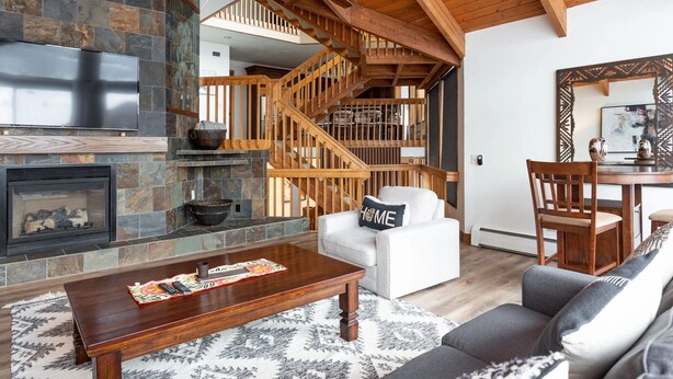 A spacious living room with a stone fireplace, wooden staircase, and a dining area with a wooden table and chairs. - Pinnacle at Deer Valley Resort - Four Bedroom Condo with Hot Tub #1263 4 Condo (Park City)