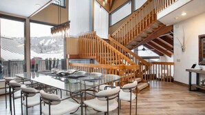 A modern dining area with a glass table and metal chairs, a wooden staircase, and large windows offering a view of the outdoors. - Pinnacle at Deer Valley Resort - Four Bedroom Condo with Hot Tub #1263 4 Condo (Park City)