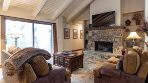A cozy living room with a stone fireplace, comfortable seating, and a large TV mounted above the fireplace.