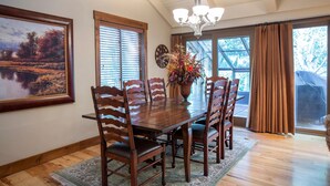 A dining room with a wooden table, chairs, a chandelier, and a large window with curtains.
