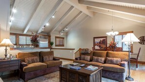 A spacious living room with a high ceiling, wooden beams, a large sofa set, a coffee table, and a floor lamp.