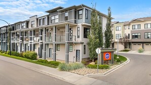 A multi-story apartment building with balconies, a landscaped front yard, and a parking area. - Lion s Den - 3bed - 5guest - 2 Smarttv - Hospital (Calgary)