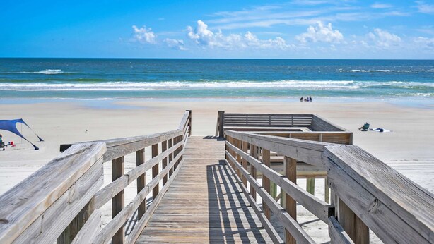 A wooden boardwalk leading to a beach with a clear view of the ocean.
