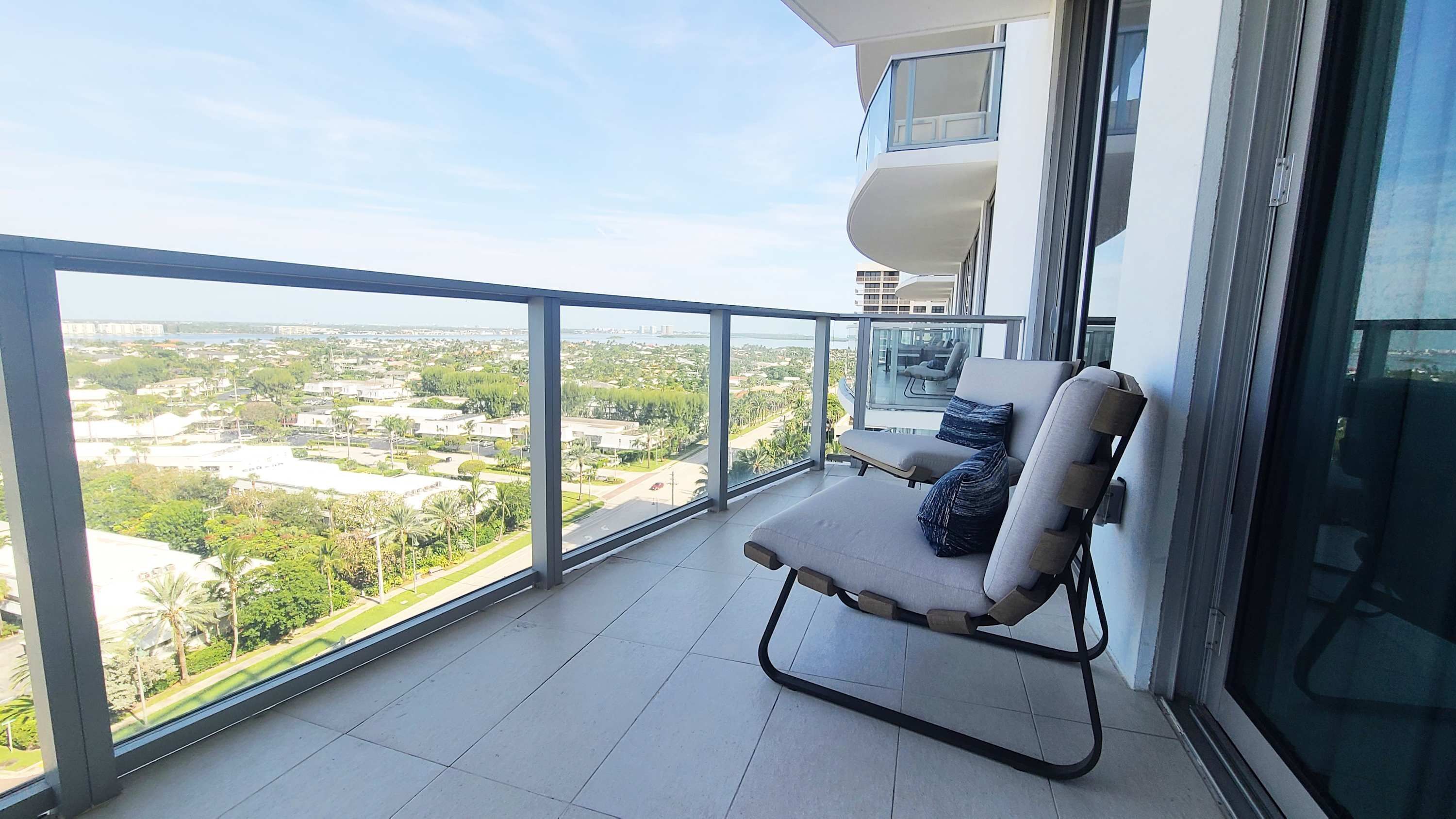 A balcony with a view of a cityscape, a cushioned chair, and a glass railing.