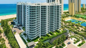 Un hotel moderno de gran altura con fachada curva, cerca de una playa y una cancha de tenis.