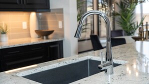Een moderne keuken met een roestvrijstalen kraan, donkere keukenkastjes en een marmeren aanrecht.