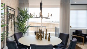 Een eetruimte met een ronde tafel, zes stoelen, een kroonluchter en een grote kamerplant.