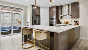 A modern kitchen with a central island, bar stools, stainless steel appliances, and a large window overlooking a balcony. - Golden Retreat - Games Movie Room - 8BD - 5bath (Calgary)