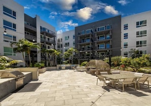 A modern outdoor patio area with stone flooring, outdoor seating, and a grill.