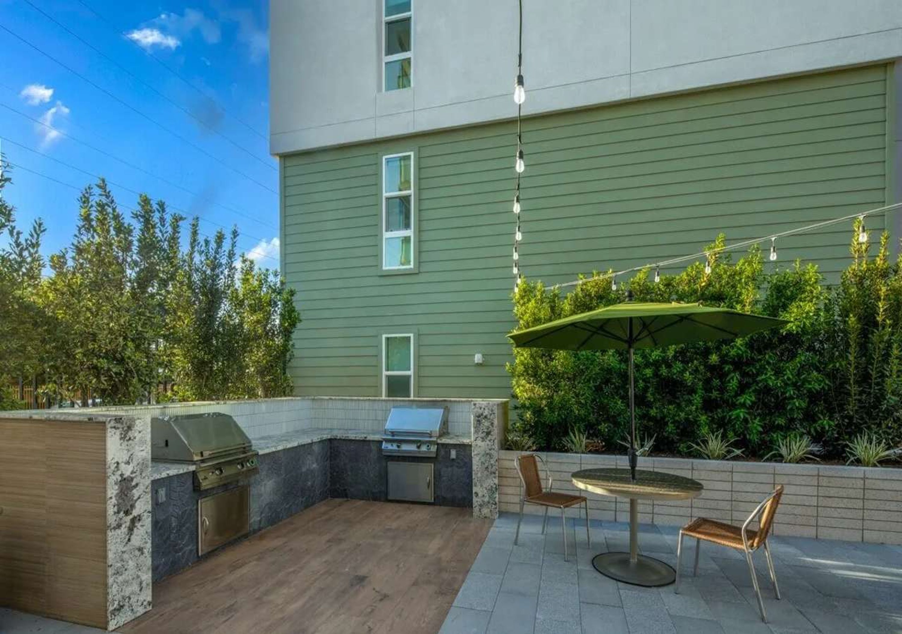 An outdoor patio with a grill, seating area, and a view of a building with a green exterior.