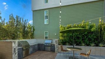 An outdoor patio with a grill, seating area, and a view of a building with a green exterior.