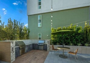 Une terrasse extérieure équipée d’un barbecue, d’un espace salon et offrant une vue sur un bâtiment à la façade verdoyante.