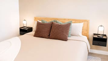 A neatly made bed with a wooden headboard, two bedside tables with lamps, and a light-colored rug.