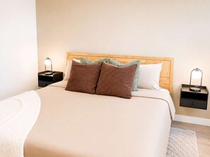Un lit bien fait, avec une tête de lit en bois, deux tables de chevet avec des lampes et un tapis de couleur claire.