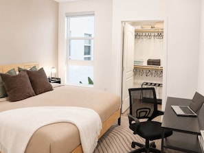 A hotel room with a bed, a desk with a laptop, a chair, a window, and a closet with hanging clothes. - Pacific Paradise 10 Min From Disneyland With Pool GYM (Santa Ana)
