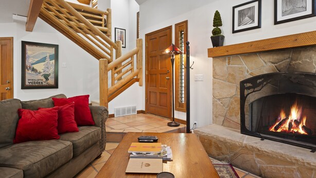 A cozy living room with a fireplace, a wooden staircase, and a sofa with red cushions.