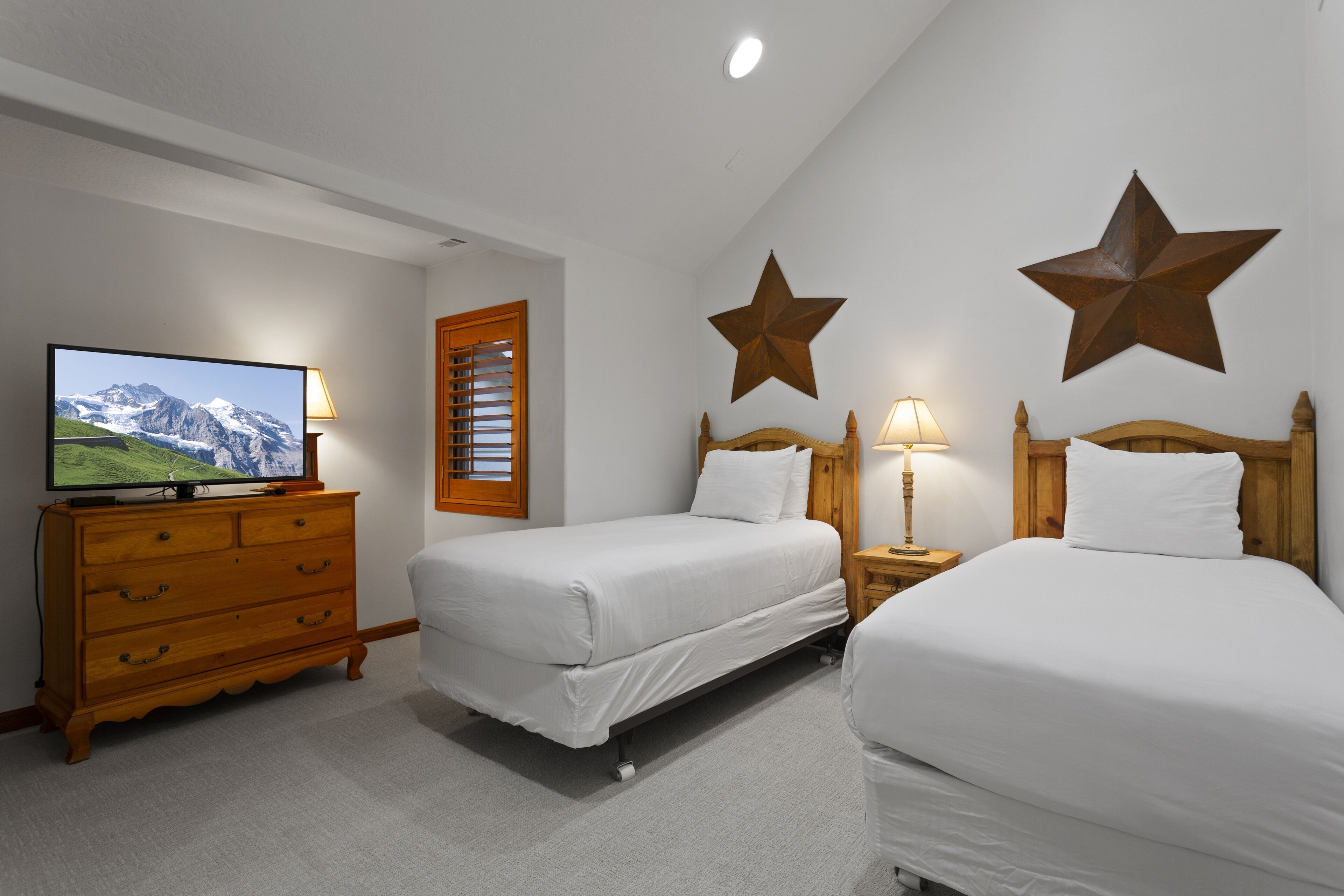 Habitación de hotel con dos camas, un aparador de madera, un televisor y decoraciones de pared con forma de estrella.