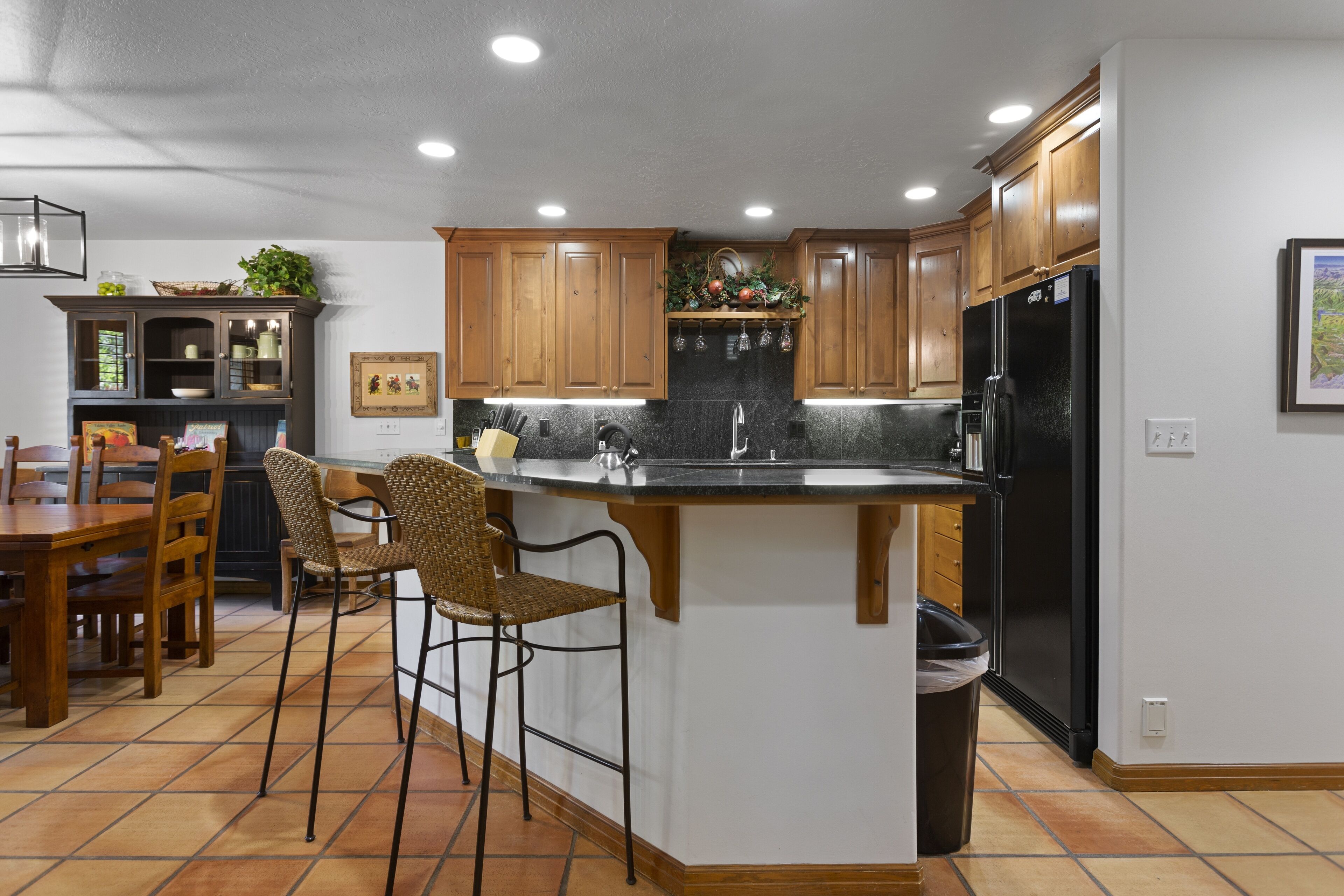 A modern kitchen with wooden cabinets, a black refrigerator, and a central island with bar stools.
