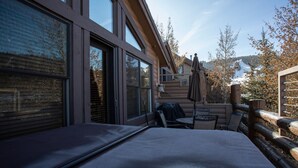 A log cabin with a large window, a covered outdoor seating area, and a view of a snowy mountain. - Comstock Lodge - Two Bedroom Condo with Hot Tub #306 by Deer Valley Resort (Park City)