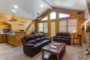 Interior de una cabaña de troncos con sala de estar, chimenea, cocina y escalera.