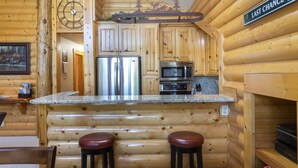 A log cabin interior with wooden walls, a kitchen area featuring stainless steel appliances, and a bar with stools. - Comstock Lodge - Two Bedroom Condo with Hot Tub #306 by Deer Valley Resort (Park City)
