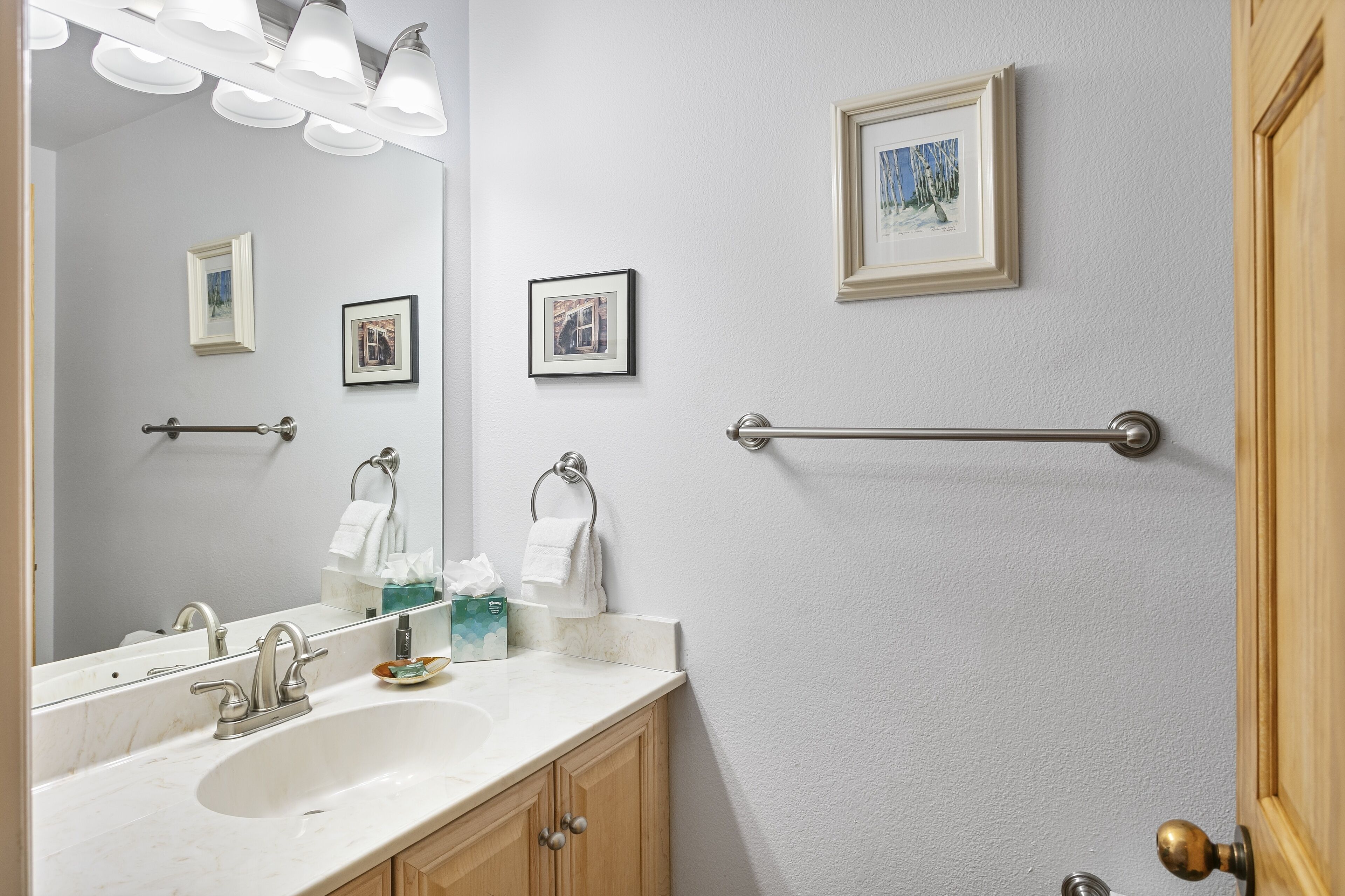 A bathroom with a sink, mirror, towel rack, and framed pictures on the wall.