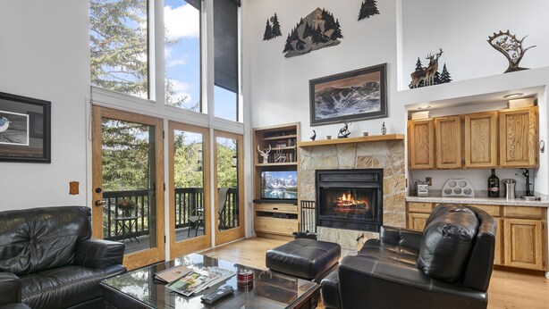 A spacious living room with a fireplace, leather sofas, a glass coffee table, and a large window overlooking a deck. - Aspenwood at Deer Valley Resort - Three Bedroom Condo with Hot Tub #1305 3 Condo (Park City)