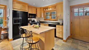 Une cuisine moderne avec des meubles en bois, un réfrigérateur noir, un îlot central doté de tabourets de bar et une grande fenêtre.