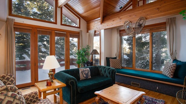 A cozy living room with a green sofa, wooden coffee table, and large windows offering a view of snow-covered trees. - Ridge at Deer Valley Resort - Three Bedroom Condo with Hot Tub #16 3 Condo (Park City)