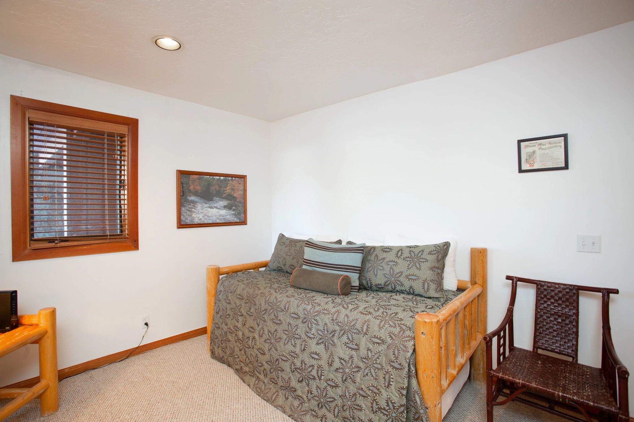 A bedroom with a wooden bed, a chair, a window with blinds, and a framed picture on the wall.