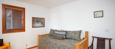 A bedroom with a wooden bed, a chair, a window with blinds, and a framed picture on the wall.
