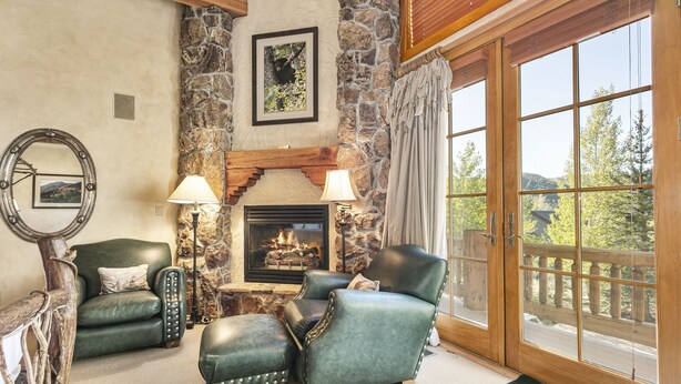 A cozy living room with a stone fireplace, leather armchairs, and a view of the outdoors.