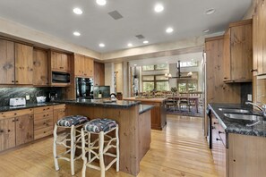 A spacious kitchen with wooden cabinets, a central island with stools, a built-in oven, and a large window providing natural light. - Thistle Drive Home at Deer Valley Resort - 4 Bedroom Home #3020 4 Condo (Park City)